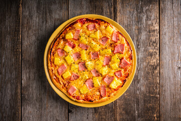 Just baked hawaiian pizza with freshly chopped pineapple and ham on the rustic wooden background. Selective focus.