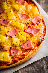 Just baked hawaiian pizza with freshly chopped pineapple and ham on the rustic wooden background. Selective focus.