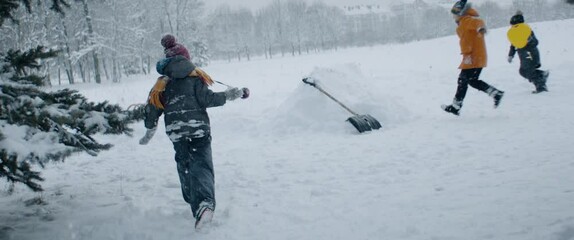 HANDHELD Group of kids friends having snowball fight, running and hiding behind the snow fort wall. Fun winter games outside. 120 FPS slow motion shot