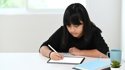 Naklejka premium Portrait of A schoolgirl using digital tablet doing homework online at home. Online education concept.