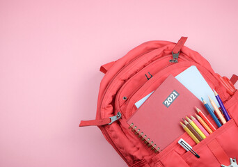  red 2021 diary in backpack with school supplies on pink background with copy space. ack  to school...