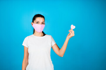Young age woman wearing coronavirus protection mask for covid-19 epidemic holding heart symbol in hand. Romantic concept.