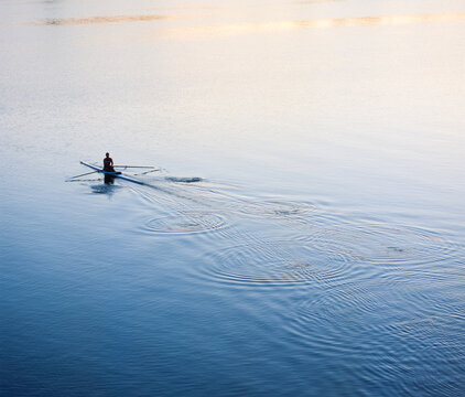 Man rowing single scull rowing boat in calm water and early morning light
