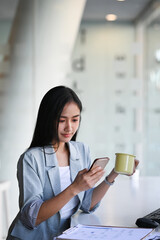 Portrait of cheerful businesswoman taking a break in office and using mobile phone.