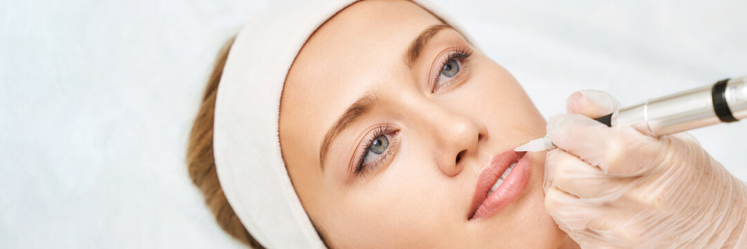 Permanent makeup. Beauty spa procedure. young woman. Face tattoo. Lip micropigmentation. Professional face microblading. Female cosmetology device. Copyspace. Mouth treatment. Dermatology