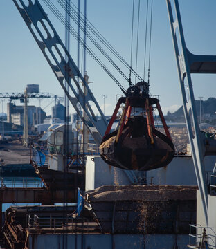Close up of large claw bucket loading wood chips onto ship at port
