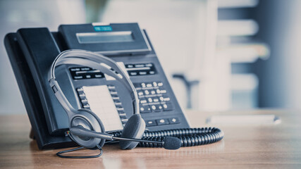 Communication support, call center and customer service help desk. VOIP headset on telephone keyboard.