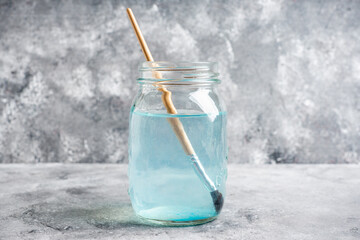 Artistic brushes in a jar with water on the gray rustic background. Artist tools. Selective focus.