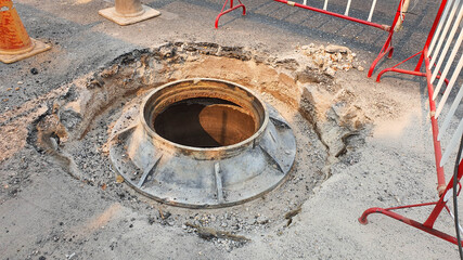 Open unsecured sewer manhole on the asphalt road. Dangerous pit on the road. Old sewer well hatch on the street