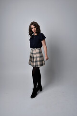 full length portrait of pretty brunette woman wearing tartan skirt and boots with long black cloak.. Standing pose holding a magical wand and casting a spell against a  studio background.