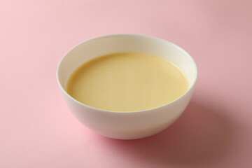 Bowl with condensed milk on pink background