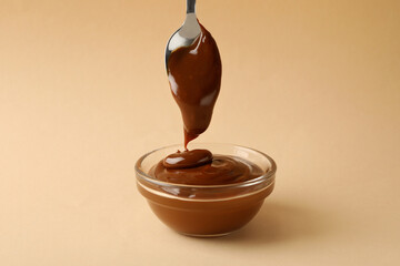Spoon and bowl with caramel condensed milk on beige background