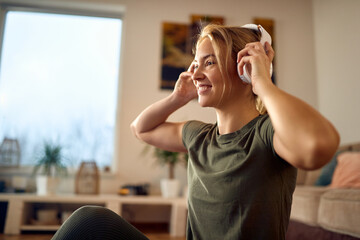 Happy athletic woman using headphones during home workout.