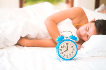 Blue vintage alarm clock on the bed at home with blurred women slepping on bed background and...