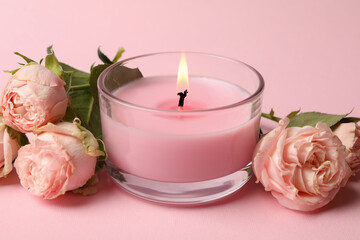 Scented candle and roses on pink background