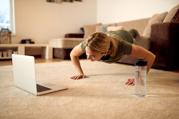 Female athlete practicing push-ups while using laptop in the living room.