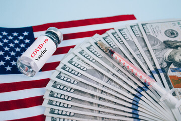Dollars bills and vial dose of COVID-19 vaccine with syringe against USA flag and blue background with copy space - global vaccination and money abuse concept. Covid vaccine cost