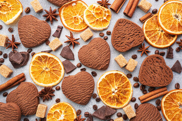 Chocolate heart cookies, oranges cinnamon and spicy spices on a gray table, top view, close up.