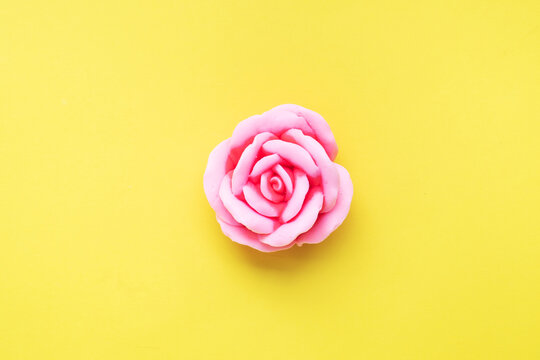 Handmade soap in the shape of a rose, pink rose flower on a yellow background. Top view, minimalist, copy space.