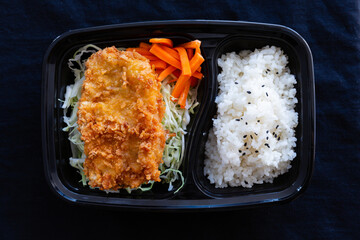 Japanese deep fried pork with rice or tonkatsu set in a lunch box on black background.