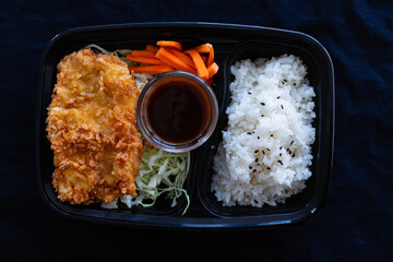 Japanese deep fried pork with rice or tonkatsu set in a lunch box on black background.