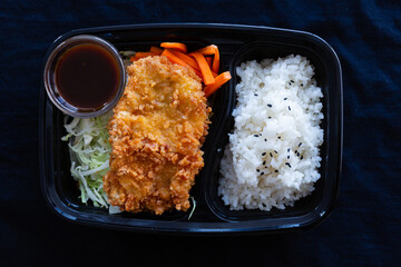 Japanese deep fried pork with rice or tonkatsu set in a lunch box on black background.