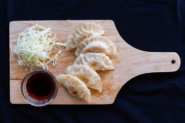 Japanese grilled gyoza dumplings with soy sauce on a wooden plate.