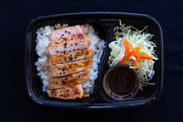 Butadon, Japanese grilled pork with rice in a lunch box on black background.