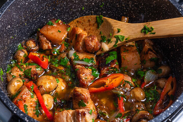 Cooking spicy pork stew with mushrooms in oriental style in a saucepan with spices, hot peppers and green onions - top view, close-up