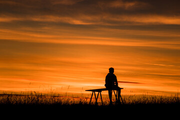 Fototapeta na wymiar adolescent en train d'admirer un coucher de soleil en été, on ne voit que sa silhouette