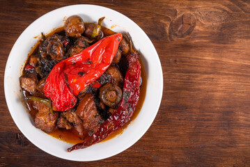 Bowl with spicy stewed pork with mushrooms in oriental style with spices, hot peppers on a wooden table - top view, copy space, close-up