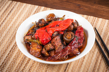 Bowl with spicy stewed pork with mushrooms in oriental style with spices, hot pepper on a bamboo napkin - top view, close-up