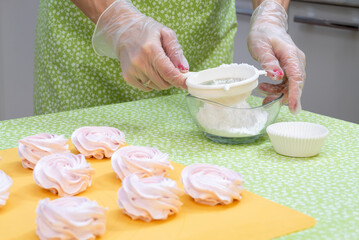 The pastry chef collects powdered sugar in a sieve before sprinkling fresh cooked marshmallows.