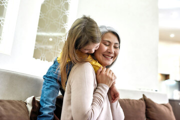 Warm hugs. Portrait of happy grandmother having fun with her joyful granddaughter while spending time together at home