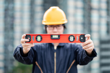 Obraz premium Asian maintenance worker man holding red aluminium spirit level tool or bubble levels at construction site. Equipment for civil engineering project