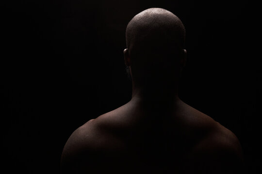 dark key photo from the back  of a black shirtless man