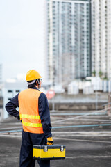 Asian maintenance worker man wearing protective suit and safety helmet carrying work tool box at construction site. Equipment for civil engineering project