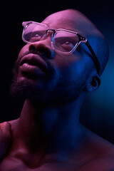 portrait of a handsome black man in red and blue light on dark background  with glasses on his eyes, he has naked sports torso