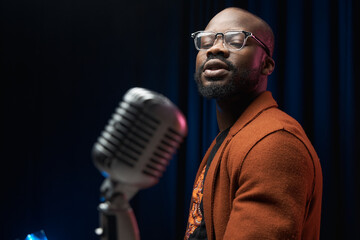 portrait of a dark-skinned handsome guy in brown jacket and black t-shirt stands with a microphone...