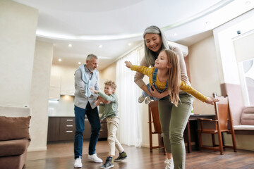 Two generations. Two excited kids, boy and girl having fun and spending time with grandparent at home