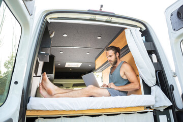 Man relaxing inside his camper van uses a laptop computer