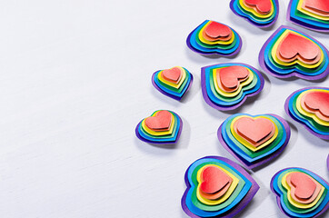 Bright rainbow hearts on white wood board, pattern, border, top view.