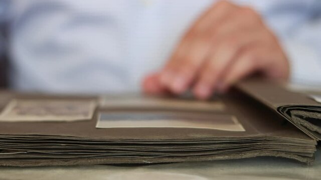 Man flips through the pages of an old album and looks through photographs.
