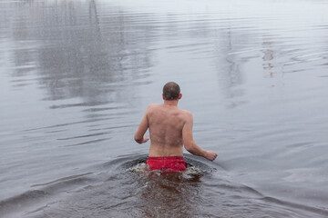 Man entering the icy water of a winter river in water baptism in the Orthodox tradition. Dnieper. Kiev. Ukraine