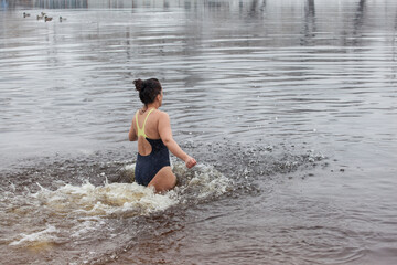 Swimming in the winter. Woman enters ice bathing water