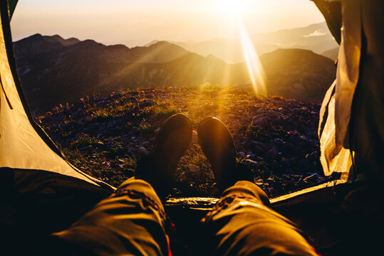 Peron's legs on doorway of camping tent near mountain during sunset