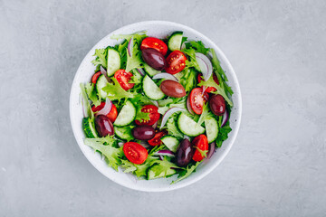 Fototapeta na wymiar Healthy green salad with fresh tomato, cucumber, red onion, olives and lettuce in bowl