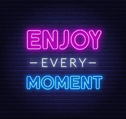 Enjoy every moment neon quote on a brick wall. Inspirational glowing lettering.