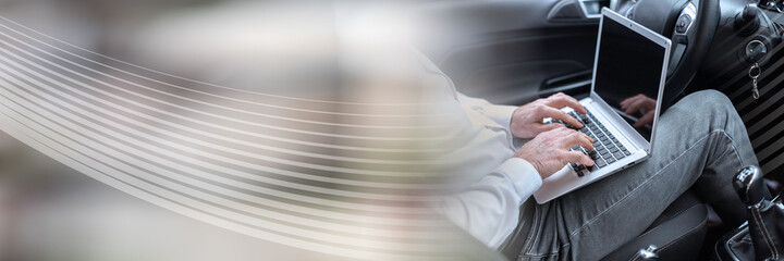 Businessman using his laptop in car; panoramic banner