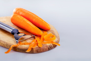Cooking healthy raw food. Peeling carrots with special knife. Raw carrot on wooden board on grey...